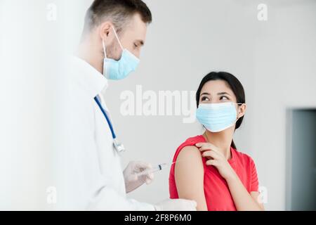 Ein männlicher Arzt im weißen Mantel hält ein Coronavirus Impfstoff in den Händen neben einem Patienten Stockfoto