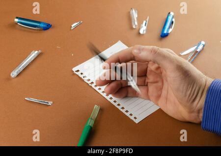 Bewegungsunschärfe. Der Erwachsene Mann spielt nervös mit dem Stift über dem braunen Schreibtisch. Defekte Stifte und leeres Blatt Papier auf der Rückseite. Konzept der Geschäftsprobleme, confl Stockfoto