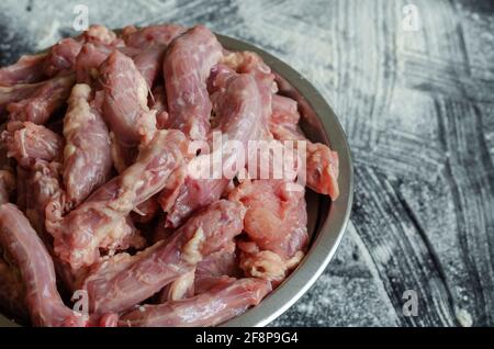 Rohe Hühnerhälse in einer Metallschüssel auf schwarzem Hintergrund. Eine volle Schüssel mit Hühnerfleisch aus Edelstahl. Essen, Zutaten. In Innenräumen. Stockfoto