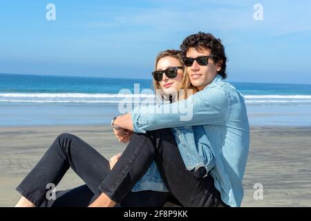 Junges Paar in Sonnenbrillen und am Strand sitzen Stockfoto