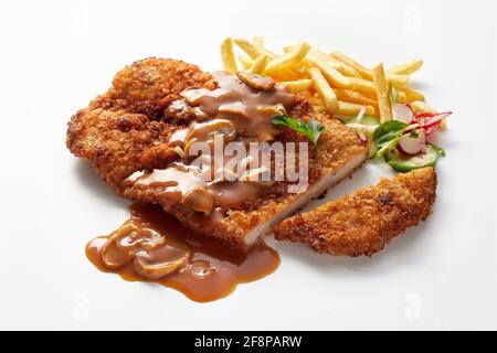 Nahaufnahme des klassischen deutschen panierten Kalbsfleischschnitzels, garniert mit chasseur-Sauce serviert mit Bratkartoffeln und Salat Stockfoto