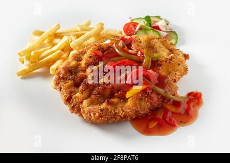 Nahaufnahme von klassischem deutschen Fleischschnitzel mit Zigeunersauce serviert Mit Bratkartoffeln und frischem Gemüsesalat auf weißem Hintergrund Stockfoto