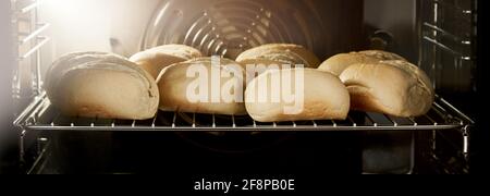 Heiße, frisch gebackene Sauerteigbrötchen mit knuspriger Kruste auf Metall Gitter im Backofen Stockfoto