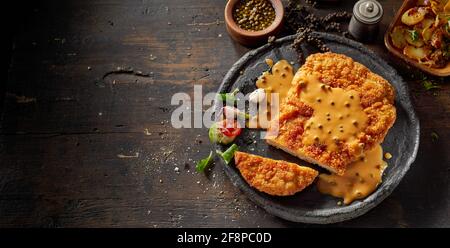 Draufsicht auf den Teller mit köstlich geschnittenem panierten Kalbsschnitzel Serviert mit Senfsoße und frischem Gemüse auf einem Holztisch Stockfoto