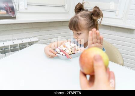 Nettes kleines Mädchen, das zwischen Äpfeln und Süßigkeiten wählen kann. Stockfoto