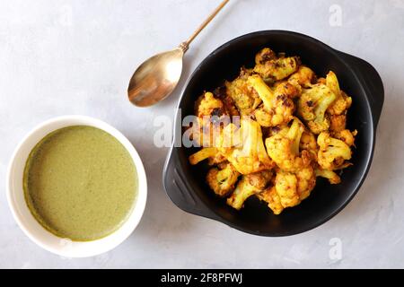 Gobi oder Gobhi Tandoori. Masala gerösteter Blumenkohl ist ein beliebtes indisches vegetarisches Vorspeise Gericht serviert mit Minze und Koriander Chutney. Stockfoto