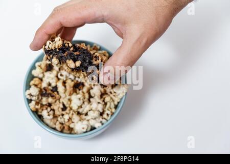 Verdorbenes verbranntes Popcorn in einer blauen Tasse. Hand des Mannes aus der Nähe Stockfoto