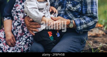 Asiatische Familie im Freien. Der Enkel sitzt auf dem Schoß seines Großvaters. Das Kind verbringt Zeit mit seinen Großeltern außerhalb der Stadt. Eld Stockfoto