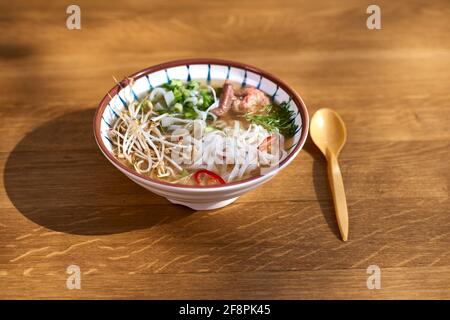 Asiatische Pho bo-Suppe, beste Pho-Brühe, in einer leichten Schüssel auf einem Holztisch. Kopierbereich, selektiver Fokus Stockfoto