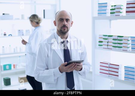 Apotheker arbeiten. Mann und Frau. Menschen Mit Spezieller Medizinischer Uniform. Mann, der das Tablet in den Händen hält. Personen in der Apotheke. Stockfoto