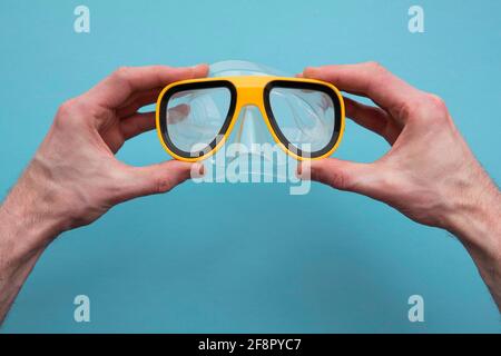 Hände, die eine gelbe Tauchmaske auf einem blauen halten Hintergrund Stockfoto