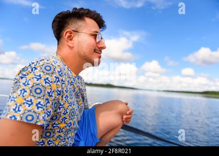 Junger Mann sitzt auf einem Hauptdeck eines Segelbootes und segelt auf einem See. Sommerferien, Kreuzfahrt, Erholung, Sport, Regatta, Freizeitaktivitäten, Service, To Stockfoto
