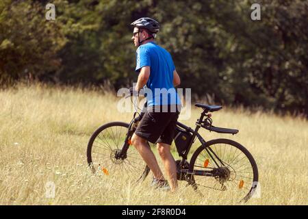 Ein Mann führt ein Fahrrad und schiebt es bergauf über eine Wiese Stockfoto