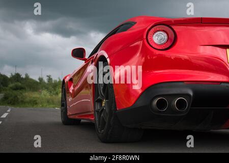 Das Heck EINES Red 2013 Ferrari F12 Berlinetta mit Glänzende Vorderräder, die bei BEWÖLKTEM Wetter die Straße hinunter schauen Tipps Für Rücklicht Und Auspuff Am Tag Stockfoto