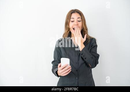 Studioaufnahme einer jungen Model-Frau im Geschäft mit grauen Hemden Kleidung isoliert auf weißen Kopienraum Hintergrund überrascht Blick auf Smartphone mit Wow expre Stockfoto
