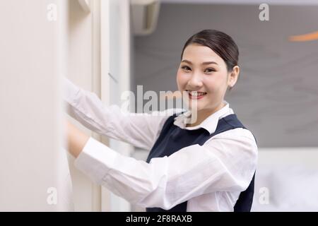 Lächelndes Zimmermädchen mit weißem Bademantel und Kleiderbügel im Kleiderschrank, das Konzept des Hotelgeschäfts Stockfoto