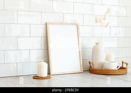 Unbeschriftete Bilderrahmen-Mockup, Rattan-Tablett mit Tasse Kaffee, Vase mit getrockneten Blumen, Kerzen. Backsteinfliesen Wand auf Hintergrund. Moderner skandinavischer Stil Stockfoto