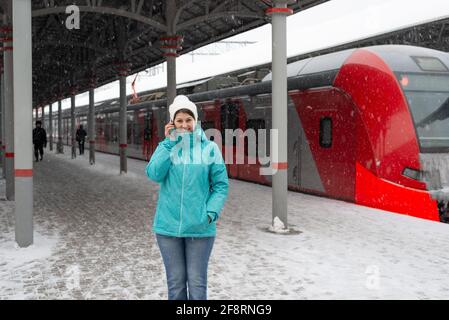 Frau mit Handy am Bahnhof im Winter während Ein Schneefall Stockfoto