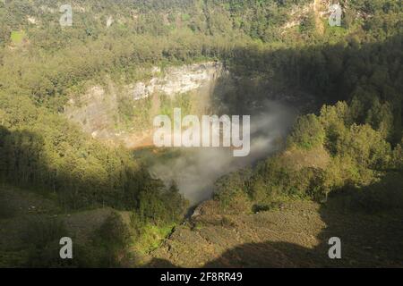 Das dunkelblaue Lagunenwasser eines der drei heiligen Seen von Kelimutu, Indonesien. Bäume umgeben den Krater, und neblige Wolken Rollen über den Krater Stockfoto