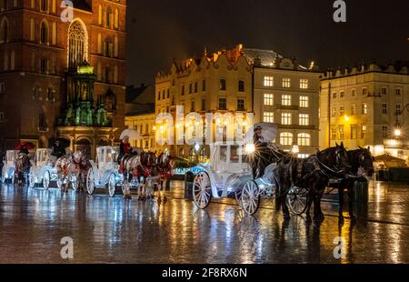 Weiße, von Pferden gezogene Kutschen warten darauf, Touristen in der Altstadt von Krakau, Polen, nachts Ausritte zu geben. Stockfoto