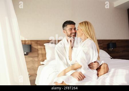 Glückliches Paar, das in einem Hotelzimmer im Bett kuschelte. Romantischer Morgen im Hotel. Ein Mann und eine Frau in weißen Roben und auf den weißen Laken eines warmen Hotels Stockfoto