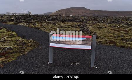 Informationstafel im vulkanischen Gebiet von Svartsengi mit Kraftwerk im Hintergrund, Fußweg und schwarzen Lavasteinen am bewölkten Wintertag. Stockfoto