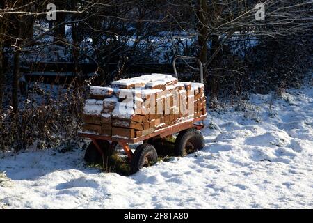 Ein Handtolley mit Ziegelsteinen beladen und mit Schnee bedeckt Ein Feld Stockfoto