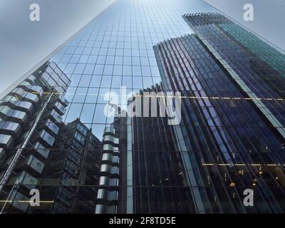 Eine Gruppe von imposanten, zyklopischen Londoner Wolkenkratzern aus Stahl und Glas, die sich in der gespiegelten Masse eines ihrer Kameraden vor einem geerdeten Himmel spiegeln. Stockfoto