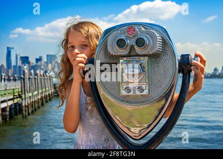 Touristenmädchen mit Fernglas in Ellis Island mit Manhattan Blick zurück in New York Stockfoto