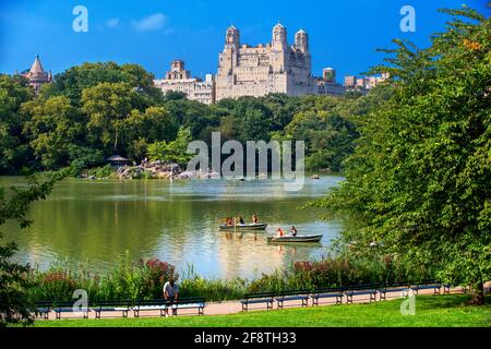 Ruderbootboote im Lake of Central Park, Manhattan New York, NY, USA. Das majestätische Gebäude am Jacqueline Kennedy Onassis Reservoir See und Upper W Stockfoto