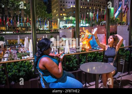 Zwei Mädchen auf der Eisbahn im Rockefeller Center und im Sommergarten Bar und Restaurant und die Statue des Titan-Gottes, Prometheus, sitzt über dem Su Stockfoto