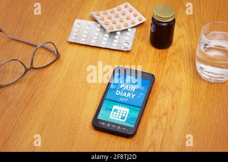M-Health-Konzept: Ein Handy, das eine mobile Anwendung mit dem Text Ihrer Schmerztagebuch-App auf einem Tisch mit Medizin, Brille und Wasser zeigt. Stockfoto