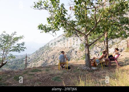 Auf einem Berg in Kotor entspannen junge westliche Reisende bei einer Erkältung Trinken Sie in der heißen Sonne, machen Sie eine Pause, genießen Sie die Aussicht von Ein Tisch draußen überschaut Stockfoto