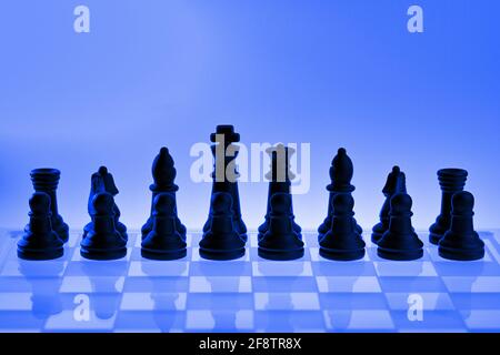 Deutschland. April 2021. Symbolische Schachfiguren eines Schachspiels aus Glas mit neutralem Hintergrund. Grundstellung der schwarzen Figuren mit blauer Lichtstimmung und Reflexionen der Schachfiguren auf dem Glasschachbrett. Credit: dpa/Alamy Live News Stockfoto