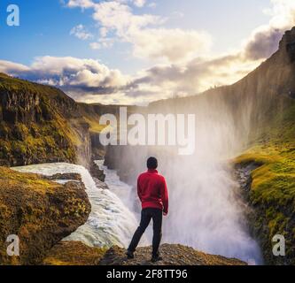 Junger Wanderer, der am Rande des Gullfoss Wasserfalls steht In Island Stockfoto