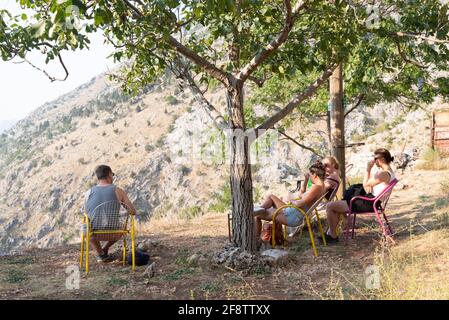 Auf einem Berg in Kotor entspannen junge westliche Reisende bei einer Erkältung Trinken Sie in der heißen Sonne, machen Sie eine Pause, genießen Sie die Aussicht von Ein Tisch draußen überschaut Stockfoto