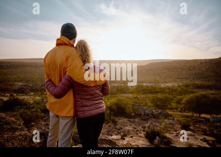 Rückansicht eines jungen Paares, das sich beim Schauen verliebt Bei schönem Sonnenaufgang nach dem Wandern zum Rand der Bergklippe Stockfoto