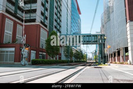 Blick auf Stadtbahngleise, die unter einem erhöhten Gehweg zwischen zwei Gebäuden in Charlotte, North Carolina, USA, verläuft Stockfoto