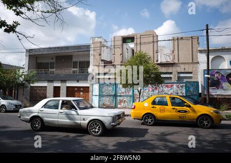 Cordoba, Argentinien - Januar 2020: Altes Oldtimer, gelbes Taxi und zerstörtes zweistöckiges Gebäude im Hintergrund. Verfallene, verfallene Häuser Stockfoto