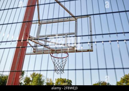 Nahaufnahme Basketballkorb gegen blauen Himmel im Stadtpark. Basketballplatz von hinten Zaun. Selektiver Fokus, unscharfer Hintergrund Stockfoto