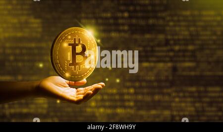Geschäftsmann hält Goldmünze Bitcoin mit binären digitalen Hintergrund. Kryptowährung und Blockchain-Technologiekonzept. Stockfoto