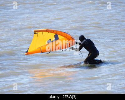 Sheerness, Kent, Großbritannien. April 2021. UK Wetter: Sonnig in Sheerness, Kent. Ein Mann versucht die neue Sportart der Tragflügeldrachen oder des "Flügelsurfens" oder "Flügelfolierung" - ein Hydrofoil-Board mit einem kleinen Drachen, den man direkt hält - anstatt die Kontrolle über mehrere Saiten und ein Geschirr wie beim traditionellen Kitesurfen zu haben. Kredit: James Bell/Alamy Live Nachrichten Stockfoto