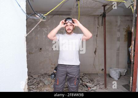 Junger Baumeister, der auf einer Baustelle eine Schutzbrille aufsetzt. Mann mit Schutzbrille. Stockfoto