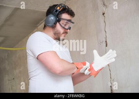 Der Baumeister legt Schutzhandschuhe an, trägt eine Schutzbrille und einen Gehörschutz. Sicherheit am Arbeitsplatz. Stockfoto
