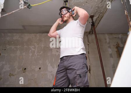 Junger Baumeister mit Gehörschutz und Schutzbrille auf einer Baustelle. Sicherheit am Arbeitsplatz. Stockfoto