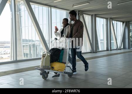 Glückliches afrikanisches Paar reist nach einer Coronavirus-Pandemie. Schwarze Passagiere im Flughafen mit Gepäck Stockfoto