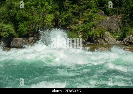 Sprudelnde Stromschnellen des Niagara River, die über Steine und Felsen fließen Mit Wald- und Felswand im Hintergrund bei Sonnenschein Wetter Stockfoto