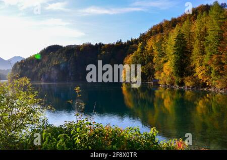 Landschaft: Blick auf einen bayerischen See, in dem sich die herbstlichen bunten Bäume am Ufer mit einem sonnigen Horizont spiegeln Stockfoto