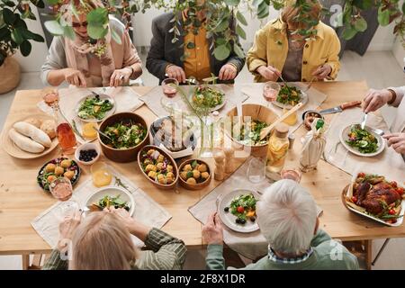 Man hat einen Blick auf die Leute, die am Esstisch sitzen Verschiedene Gerichte und gemeinsames Abendessen Stockfoto