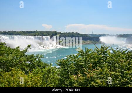 Blick zwischen Bäumen auf die kanadischen und amerikanischen Niagarafälle Mit Touristenboot auf dem Wasser bei sonnigem Wetter Stockfoto